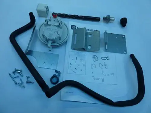 Set bestehend aus verschiedenen Bauteilen, darunter ein Luftdruckwächter von Remeha, Metallelemente, Schläuche und Montageanleitungen auf einem weißen Hintergrund.